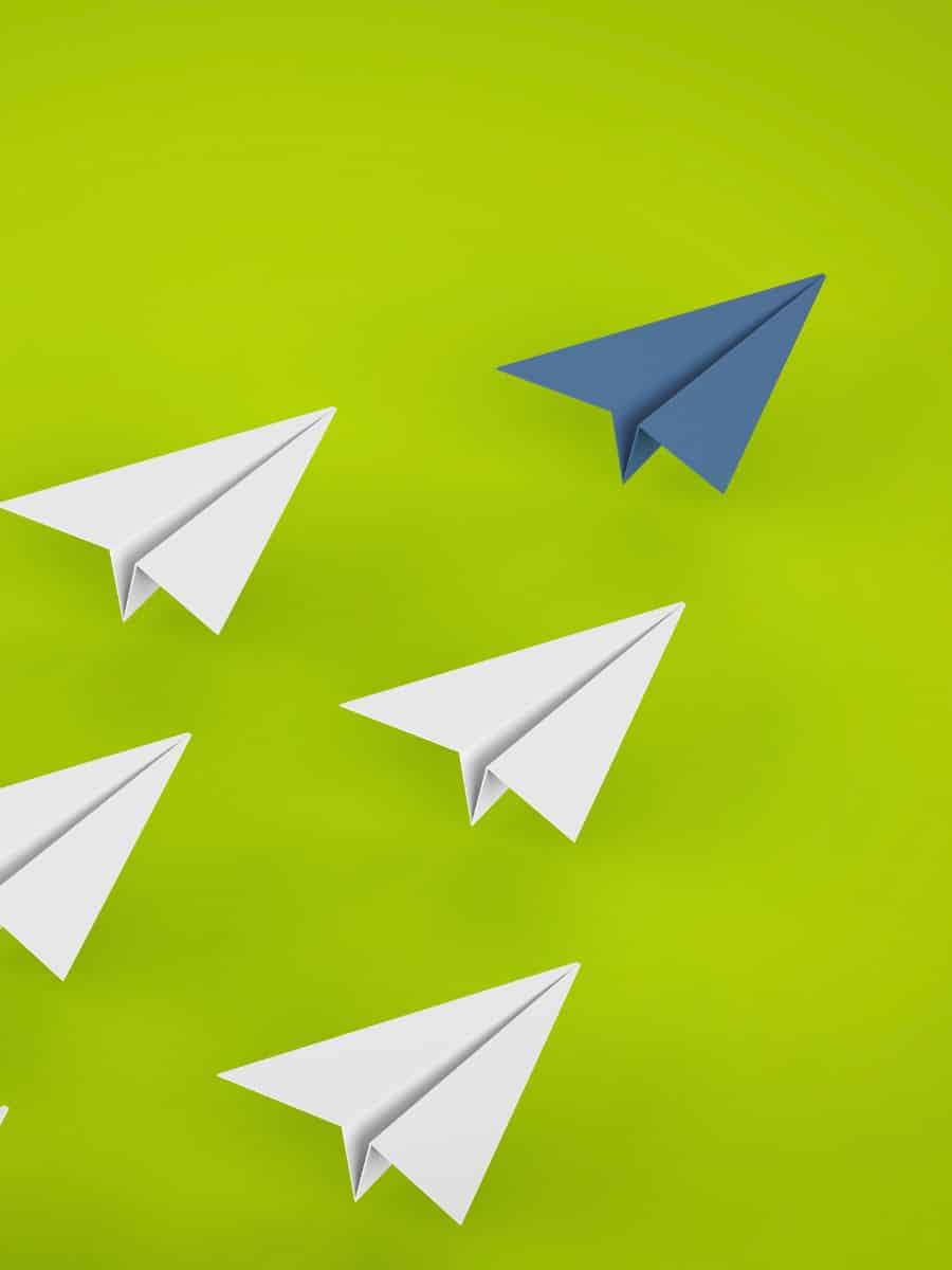 a formation of five paper airplanes — four are white, the leader is blue — against a lime green background