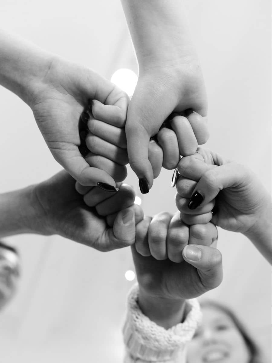 hands of five people, each forming a fist, placed into the center of the frame; black and white