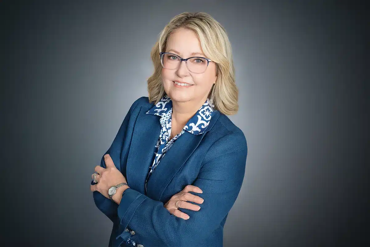 Priscilla's Headshot - blond woman standing with her arms crossed, she's wearing a blue blazer and has glasses